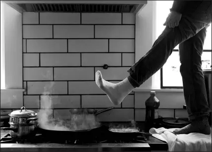  ?? ASHLEY LANDIS / ASSOCIATED PRESS FILE (2021) ?? A man stands on his kitchen counter to warm his feet over his gas stove during a snow storm Feb. 16, 2021, in Austin, Texas. Following comments made by a member of the Consumer Product Safety Commission on Jan. 9, misleading claims that the Biden administra­tion is planning on banning gas stoves have spread widely across social media platforms.