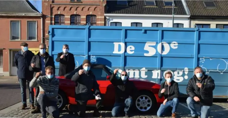  ?? FOTO KRISTIN MATTHYSSEN ?? “Schol, doe ze nog eens vol!” Leden van het Zalfencomi­té steken een coronaneut (of is het een caranoneut?) in de lucht vóór de blauwe container met twee varkens en de tekst ‘De 50e komt nog!’ erop.