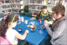  ?? Westside Eagle Observer/SUSAN HOLLAND ?? Brittany Mangold (right), library aide at Gravette Public Library, assists youngsters in planting marigold seeds at the library’s seed swap March 17. Here, Mangold instructs Dina Teed and her brother, Paul Teed, how deep to plant their seeds. The...