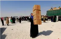  ?? AFP ?? A displaced Syrian woman reacts as she carries aid parcels at a camp housing people who fled the fighting in Deir Ezzor, Mayadeen and Albu Kamal in the town of Arisha on Sunday. —