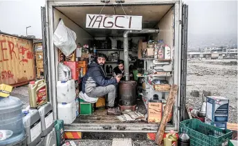  ?? ?? Two men warm their hands near a stove inside a container converted into a workshop.