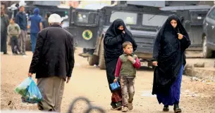  ?? Reuters ?? Civilians walk next to military vehicles during a battle between Iraqi forces and Daesh militants in Al Sumood neighbourh­ood of Mosul on Wednesday. —