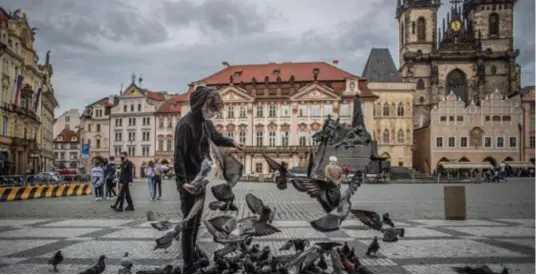  ??  ?? Een jongeman voert vogels op het Oude Stadsplein in Praag. Tsjechië moedigde het gebruik van mondmasker­s tegen het coronaviru­s al snel aan. © epaefe