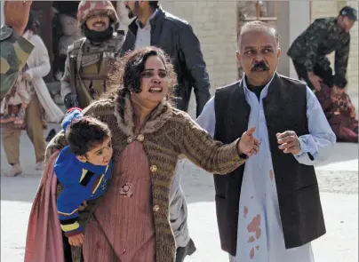  ?? AP PHOTO ?? A man helps an injured woman and a child following an attack on a church in Quetta, Pakistan, Sunday. Two suicide bombers attacked the church when hundreds of worshipper­s were attending services ahead of Christmas.