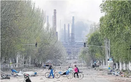  ?? REUTERS ?? People walk their bikes across the street as smoke rises above Azovstal Iron and Steel Works in Mariupol on Monday.