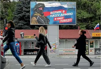  ?? AP ?? People walk past a pro-russian billboard reading, ‘‘We believe in our army and our victory’’ in Luhansk, as they await the results of a referendum on whether Russian-occupied regions in eastern Ukraine should be annexed by Moscow.