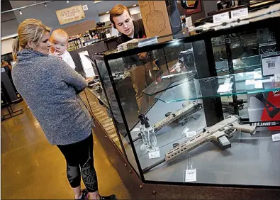  ?? AP/CHARLIE RIEDEL ?? A salesman points out features on a handgun for Anne Vifquain while she holds her son Gavin at the Frontier Justice store in Lee’s Summit, Mo., earlier this month.