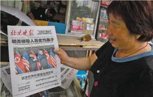  ?? NG HAN GUAN ASSOCIATED PRESS ?? A newspaper vendor at a newsstand in Beijing holds up a front page photo on Tuesday of the meeting in Singapore between President Donald Trump and North Korean leader Kim Jong Un. As Kim returns on a plane China provided him for the Singapore trip,...