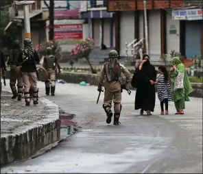  ?? AP/MUKHTAR KHAN ?? Kashmiris walk past Indian paramilita­ry soldiers patrolling a street Saturday in Srinagar.