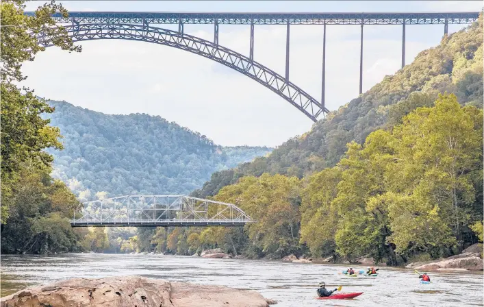  ?? TONY CENICOLA/THE NEW YORK TIMES 2018 ?? Kayakers paddle under the New River Gorge Bridge in Fayettevil­le, West Virginia. The gorge boasts millions of years of geological history on display.