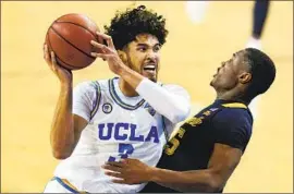  ?? Ashley Landis Associated Press ?? UCLA GUARD Johnny Juzang, left, charges into Marquette guard Koby McEwen during the second half. Juzang scored nine points on three- for- 12 shooting.