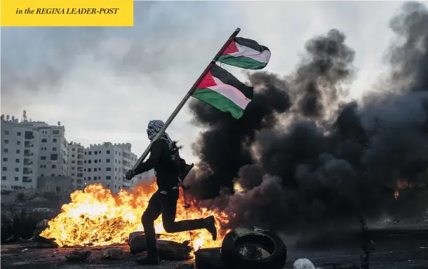  ?? CHRIS MCGRATH / GETTY IMAGES ?? A protester runs past a burning barricade carrying a Palestinia­n flag during clashes with Israeli border guards near a checkpoint in Ramallah, West Bank, on Saturday. Protests and clashes continued across Jerusalem and the West Bank following U.S....