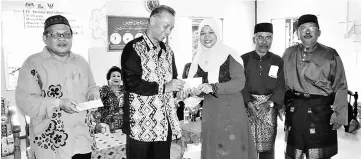  ??  ?? Dr Penguang (second left) presenting ‘duit raya’ to one of the villagers. With him from left are Mazlan and Said.