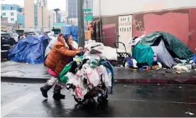  ?? California. Photograph: Frederic J Brown/AFP/Getty Images ?? A homeless woman pushes her belongings past a row of tents on the streets of Los Angeles,