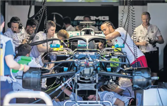  ??  ?? El piloto británico Lewis Hamilton observa cómo sus mecánicos trabajan en el Mercedes dentro del garaje del equipo alemán.