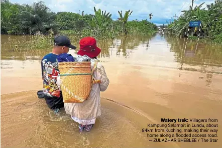  ?? ?? Watery trek: Villagers from Kampung Selampit in Lundu, about 84km from Kuching, making their way home along a flooded access road. — Zulazhar Sheblee / The Star