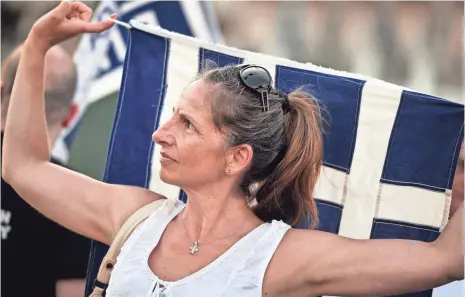  ?? LOUISA GOULIAMAKI, AFP/GETTY IMAGES ?? A woman holds a Greek flag in front of the Parliament in Athens during an anti-EU demonstrat­ion Monday.