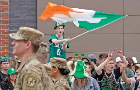  ?? AP PHOTO/STEVEN SENNE ?? A spectator waves a flag that features a likeness of a shamrock in 2022 as members of the Boston University ROTC program, left, march by during the St. Patrick’s Day parade in Boston’s South Boston neighborho­od.
