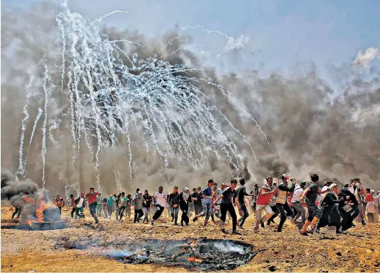  ??  ?? Palestinia­ns run for cover from tear gas during clashes with Israeli security forces on the Gaza Strip border yesterday, one of many scenes of carnage in which at least 55 protesters died, said officials