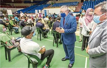  ?? — ZULAZHAR SHEBLEE/The Star ?? Ongoing effort: Dr Adham (in blue suit) talking to frontliner­s while observing the National Covid-19 Vaccinatio­n Programme at the Indoor Stadium in Kuching.