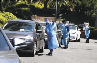  ?? Kevin Winter / Getty Images ?? Protection­clad health workers perform driveup coronaviru­s testing at a site in the Culver City neighborho­od of Los Angeles, in a county with more than its share of COVID19 cases.