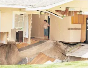  ?? STEPHEN M. DOWELL/STAFF PHOTOGRAPH­ER ?? Ellen Miller carefully surveys the damage as her home on West Kelly Park Road in Apopka is swallowed by a sinkhole Tuesday. She and her husband, Garry, had lived in the home for 49 years.