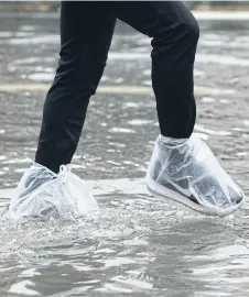  ?? PatiPat Janthong ?? right A resident finds a novel way to keep shoes dry while walking through floodwater, by wrapping them in plastic bags, on Lat Phrao Soi 23.