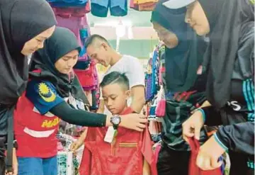  ??  ?? HAZIQ Azizi dibantu rakannya memilih baju raya dalam program anjuran HIKMAH Cawangan Sarikei.