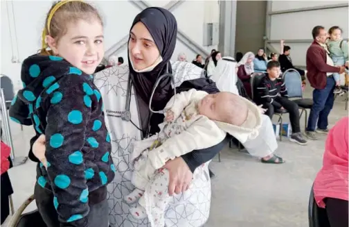  ?? WAM ?? ↑
An Emirati official receives Palestinia­n children at the Abu Dhabi Internatio­nal Airport on Wednesday.