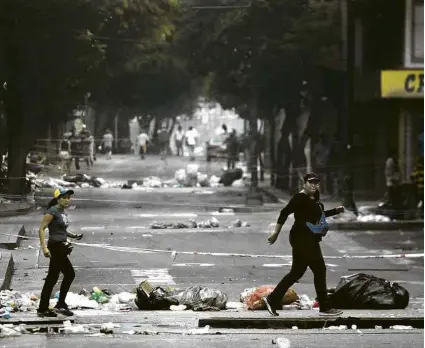  ?? Carlos Garcia Rawlins - 30.jul.2017/Reuters ?? Mulheres cruzam rua de Caracas repleta de entulho após um protesto contra a eleição da Assembleia Constituin­te