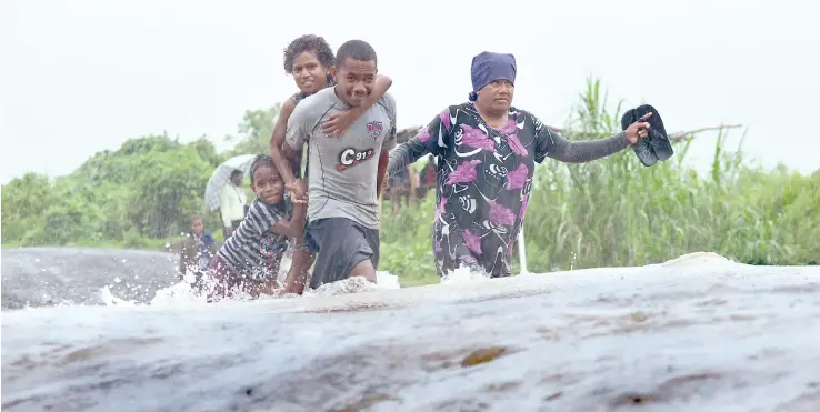  ?? Photo: Jone Luvenitoga ?? In the flood yesterday: Anameli Marama gets a piggy back ride on Iliaseri Mataturaga as Eta Bote (left), holds on. On the right is Karalaini Soli, crossing the flooded Nailawa bridge at Dawasamu, Tailevu.