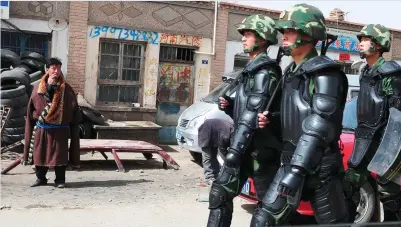  ??  ?? ILLEGAL OCCUPATION: A Tibetan man looks on as Chinese paramilita­ry troops in riot gear march into his town