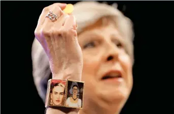  ??  ?? La premier Theresa May con un braccialet­to «Frida Kahlo» mostra la caramella offertale contro l’attacco di tosse