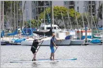  ??  ?? STUDENTS learn the basics on the sand, top, before venturing out on the water, where Tim Sanford, above right, owner of Paddle Method, schools a beginner in the art of paddle-boarding.