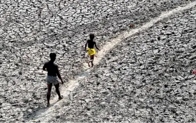  ?? AP ?? A man and a boy walk across the bed of the driedup Yamuna River in New Delhi. A World Meteorolog­ical Organisati­on report says the world is getting closer to the 1.5C warming threshold that agreements are trying to prevent.