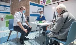  ?? VICTORIA JONES GETTY IMAGES ?? Sir Simon Stevens, chief executive of the NHS in the U.K., talks with a patient at a vaccinatio­n centre. Two people have had a severe reaction, but recovered.