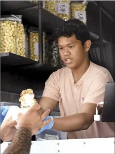  ?? The Maui News / MATTHEW THAYER photos ?? Aloha Kettlecorn & Ice Cream food truck cashier Caivin Llanos serves a cup of “fruity shells” to a customer Wednesday afternoon at the Maui Street Market on Hana Highway in Kahului.