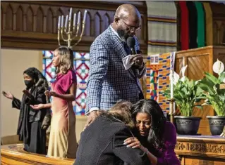  ?? ?? Above: The Revs. William H. Lamar IV (standing) and Cozette Thomas (right) pray with a parishione­r during Palm Sunday services at the Metropolit­an AME Church. Lamar says Black Protestant churches are still feeling the pandemic’s impact on attendance.