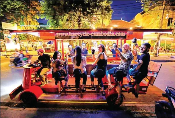  ?? HONG MENEA ?? Not quite a tuk-tuk, nor a food truck, the bar-on-wheels turns heads as it drives down the street with its bar stools and open design, thumping music and revellers enjoying themselves.