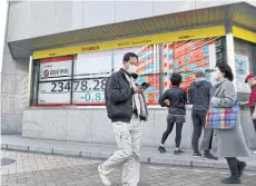  ?? AFP ?? Pedestrian­s walk past an electric quotation board displaying the Nikkei 225 Index on the Tokyo Stock Exchange in Tokyo on Friday.