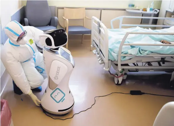  ?? AP ?? Flavio Tangian, subjefe de la Unidad de Cuidados Intensivos de un hospital en Varese, Italia, prepara a un robot que asiste al personal con el monitoreo de los pacientes con covid-19. En ese país, el número de enfermos graves por esta enfermedad ha ido disminuyen­do.