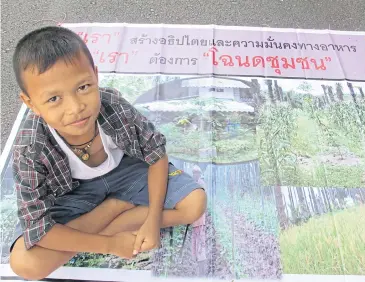  ?? SANITSUDA EKACHAI ?? A boy sits on a poster calling for community rights to manage forest land use during one of the street protests.