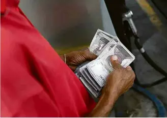  ?? Marco Bello/Reuters ?? Venezuelan­o conta notas em posto de combustíve­l de estatal em Caracas