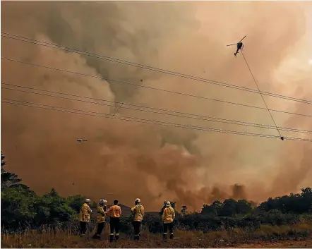  ?? SYDNEY MORNING HERALD ?? Firefighte­rs watch nervously as helicopter­s with monsoon buckets battle the Gospers Mountain fire northwest of Sydney. Over 200 additional trucks and firefighte­rs have been brought in to fight the six major wildfires across New South Wales.