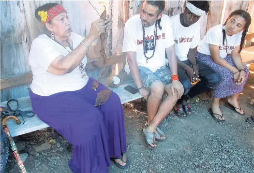  ??  ?? Taino elder Vanessa Inaru Pastrano inspects a piece of local tobacco given to her while Luis Cozcacuauh­tli of Mexico, Kemoy Blake of Portland, and Xitlalin Payan of California look on.