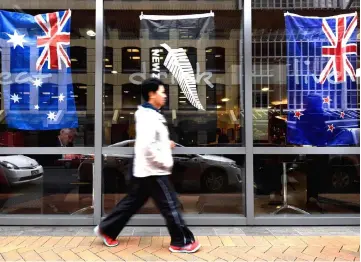  ?? — AFP photo ?? File photo shows a pedestrian walking past a bar window displaying New Zealand’s national flag (right) and Australia’s national flag (left) in Wellington, ahead of the Rugby World Cup final match played in Twickenham, England between the two countries.