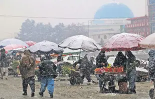  ?? ?? Pedestrian­s pass street vendors as snow falls in Kabul, Afghanista­n, Jan. 3, 2022.