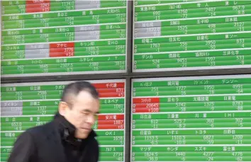  ?? — AFP ?? A businessma­n walks past an electric quotation board flashing share prices of the Tokyo Stock Exchange (TSE) in front of a securities company in Tokyo.