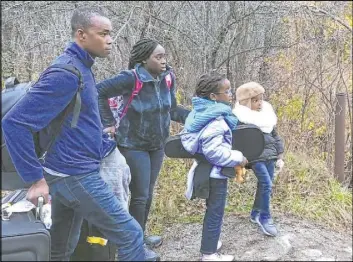  ?? Wilson Ring The Associated Press ?? A family from Nigeria waits Monday in Champlain, N.Y., to illegally cross the U.S. border into Canada, where Royal Canadian Mounted Police officers wait.