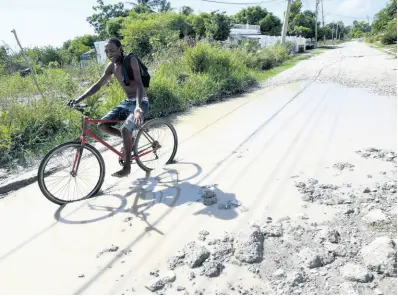  ??  ?? A pedal cyclist rides through a flooded roadway in Willowdene Estates, St Catherine, yesterday, where residents are calling on the authoritie­s to address the poor road conditions.